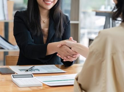 businesspeople shake hand after their partnerships in conference room and finalized pile of papers of financial report and data analysis on meeting table.